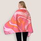 A woman wearing a pink swirls print fleece cape blanket, draping comfortably over her shoulders. The stylish and cozy wrap features a marbled pink and orange pattern, ideal for warmth and fashion.